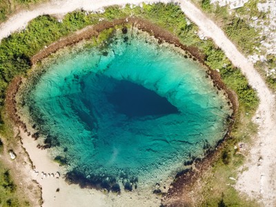 een helderblauw karstmeer met diep donker centrum, omringd door wandelpaden in Kroatië.