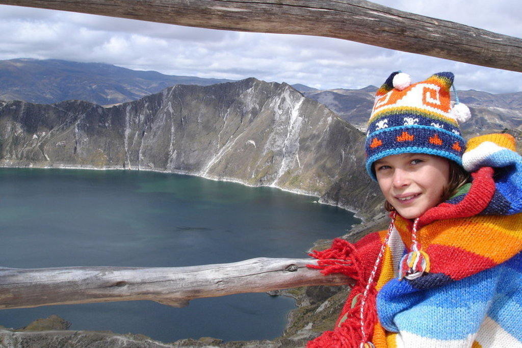 Kind in kleurrijke poncho bij uitzichtpunt over het Quilotoa-kratermeer in Ecuador.