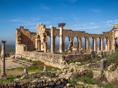 Ruïnes van de Romeinse stad Volubilis langs de Route Marokko, met bogen en zuilen onder een blauwe lucht.