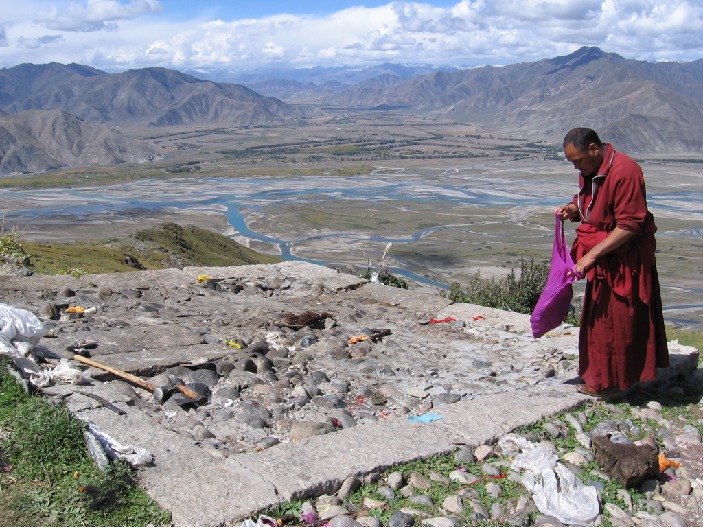 Boeddhistische monnik kijkt uit over een rivierdelta en bergen in Tibet, tijdens groepsrondreis Tibet en Nepal.