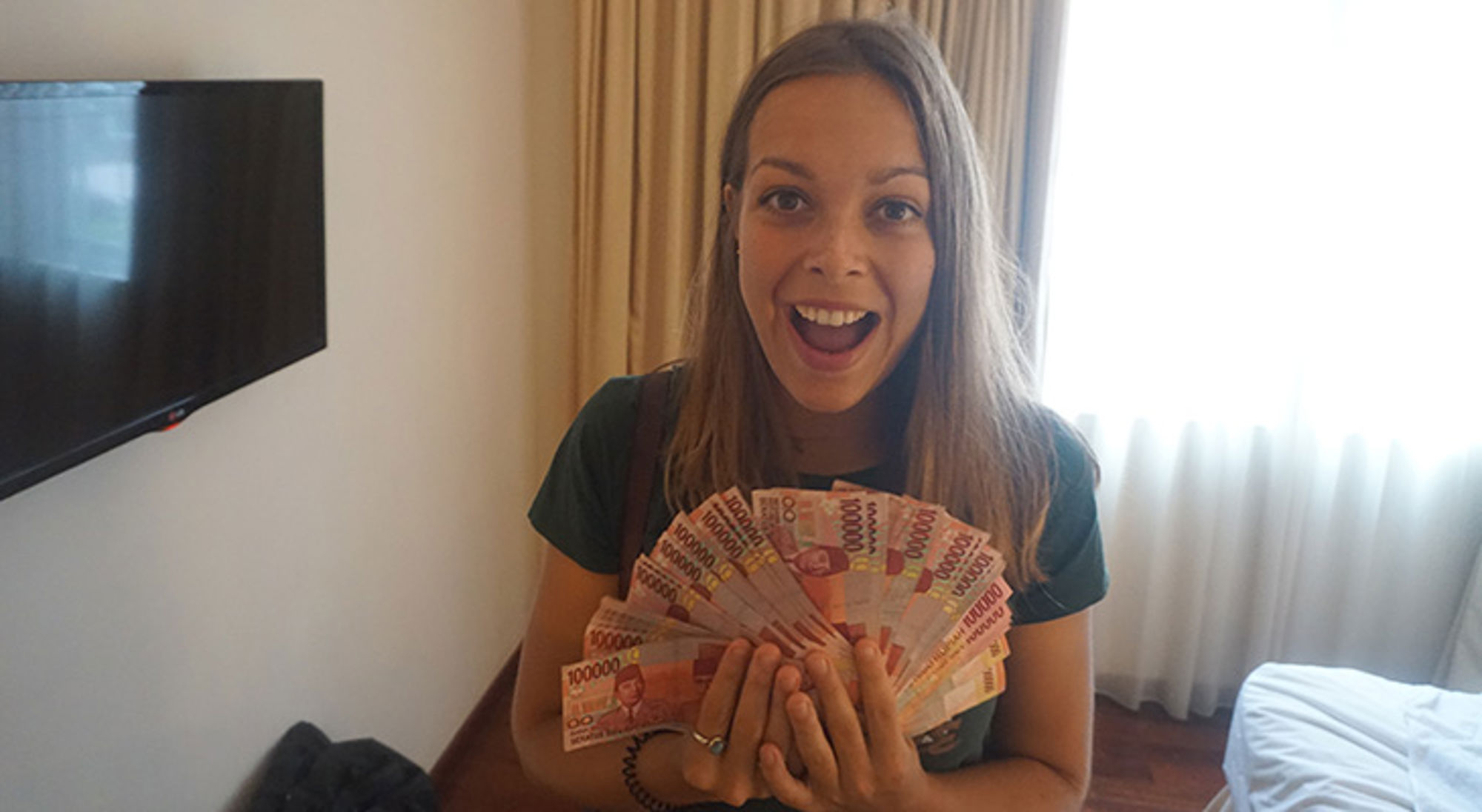 Vrouw houdt een waaier van Vietnamese dongbiljetten vast en lacht in een hotelkamer.