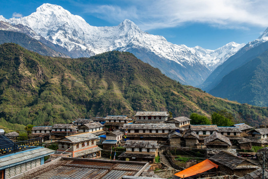 Dorp in de Himalaya in Nepal met traditionele huizen en besneeuwde bergtoppen op de achtergrond.