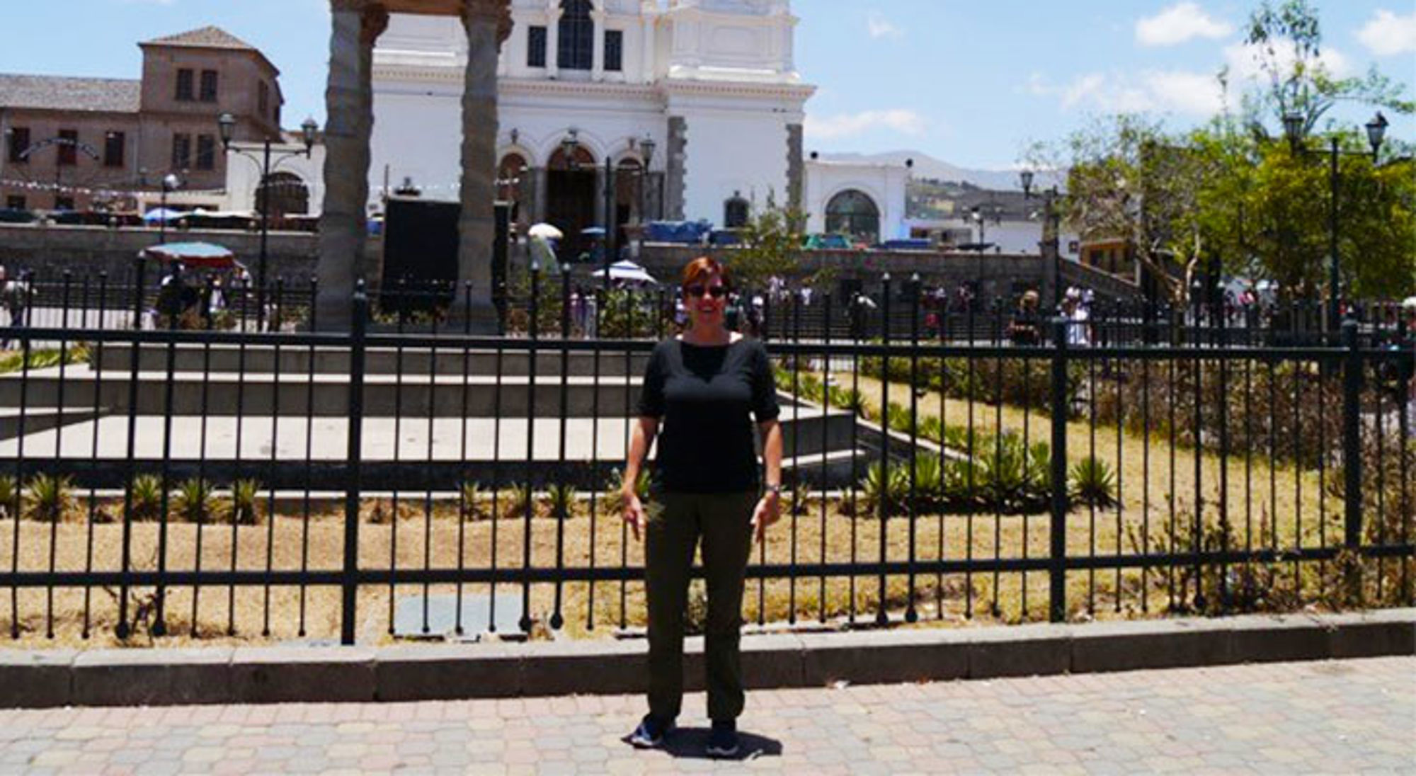 Annegien in Ecuador Reiziger poseert voor een witte kathedraal op een druk plein met palmbomen.