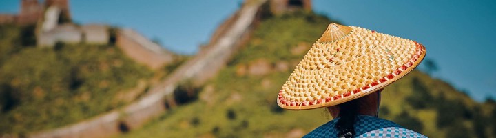 Reiziger met rieten hoed kijkt uit op de Chinese Muur tijdens een rondreis door Azië.