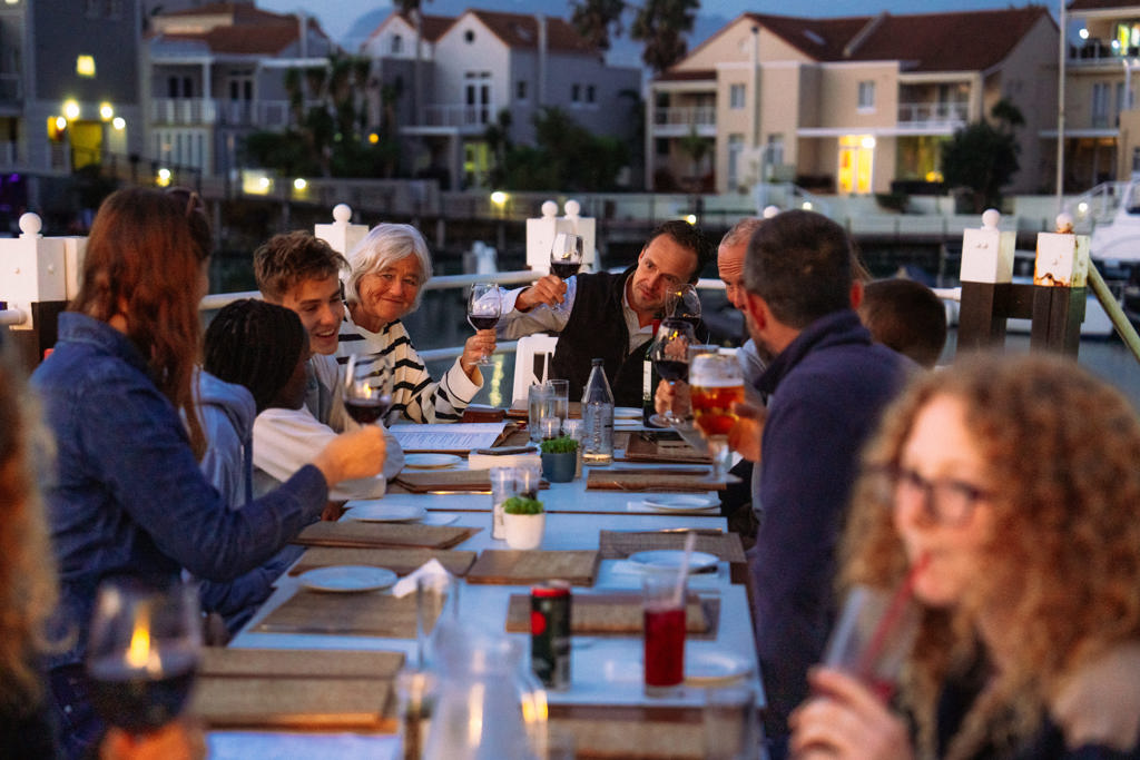 Gezin dineert aan het water en proost met wijn tijdens familiereis Zuid-Afrika Tuinroute & Kruger.