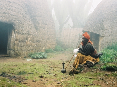 Man met waterpijp bij traditionele ronde hutten in een mistig dorp in Ethiopië.