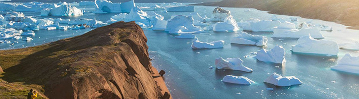 Uitzicht op drijvende ijsbergen in een fjord bij zonlicht, gezien vanaf een rotsachtige kust.