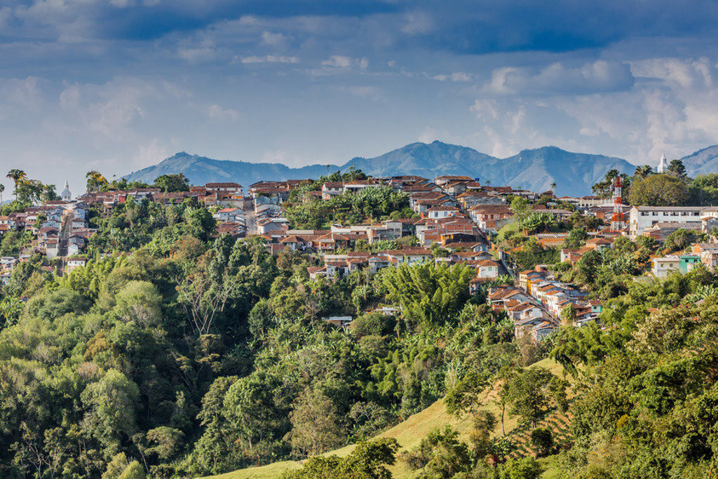 Uitzicht op een bergdorp in Colombia met kleurrijke huizen, groene heuvels en bergen op de achtergrond.