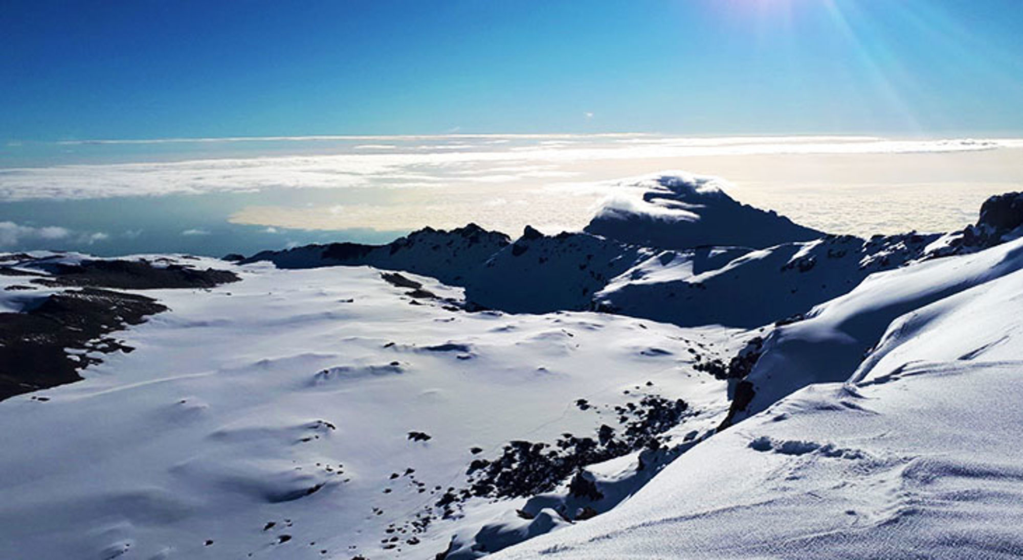 Besneeuwd berglandschap met bergkam boven een wolkendek onder een heldere blauwe lucht.