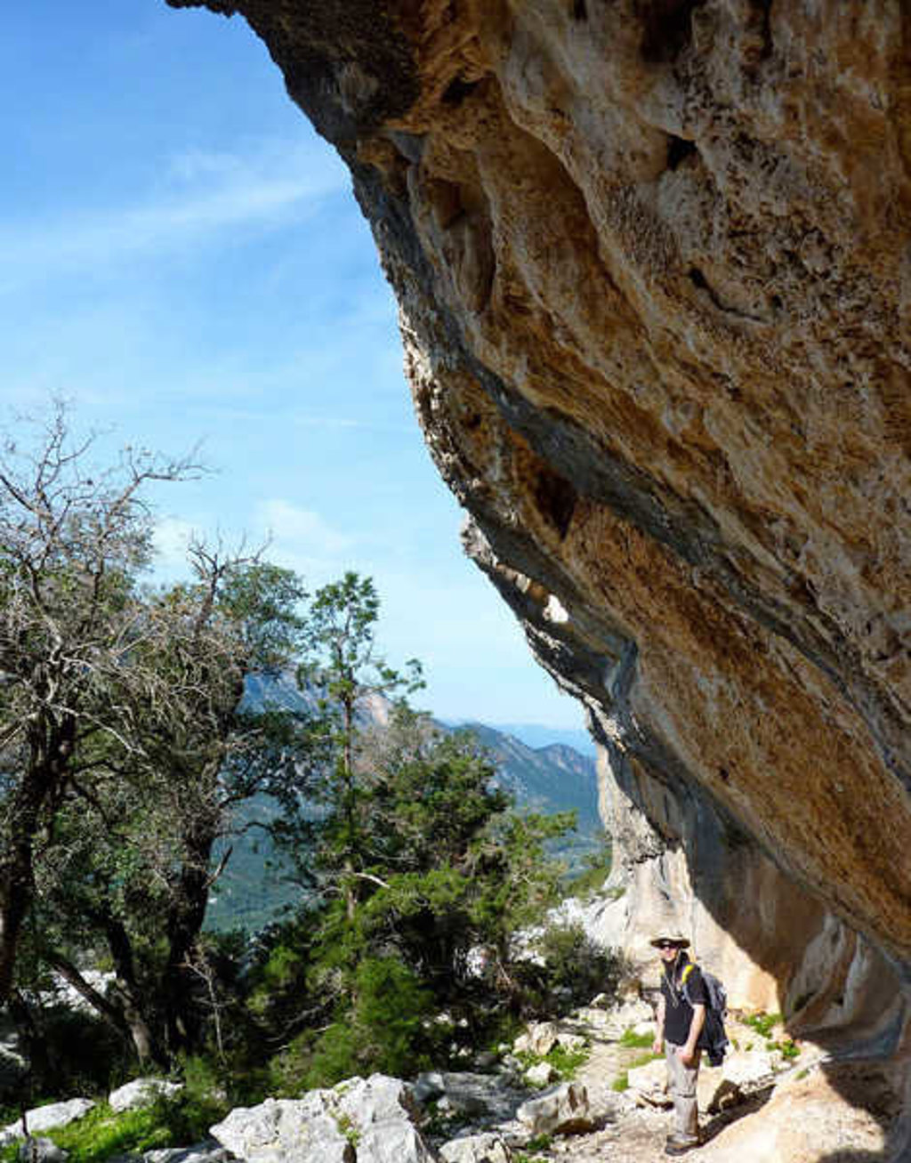 Wandelaar op rotsig pad onder een grote overhangende rotswand in Sardinië, Italië.