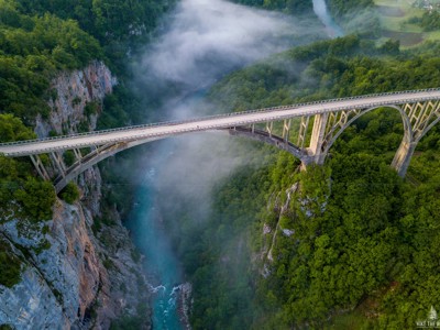 Boogbrug over een diepe rivierkloof met nevel, langs de Route Zuidoost Europa.