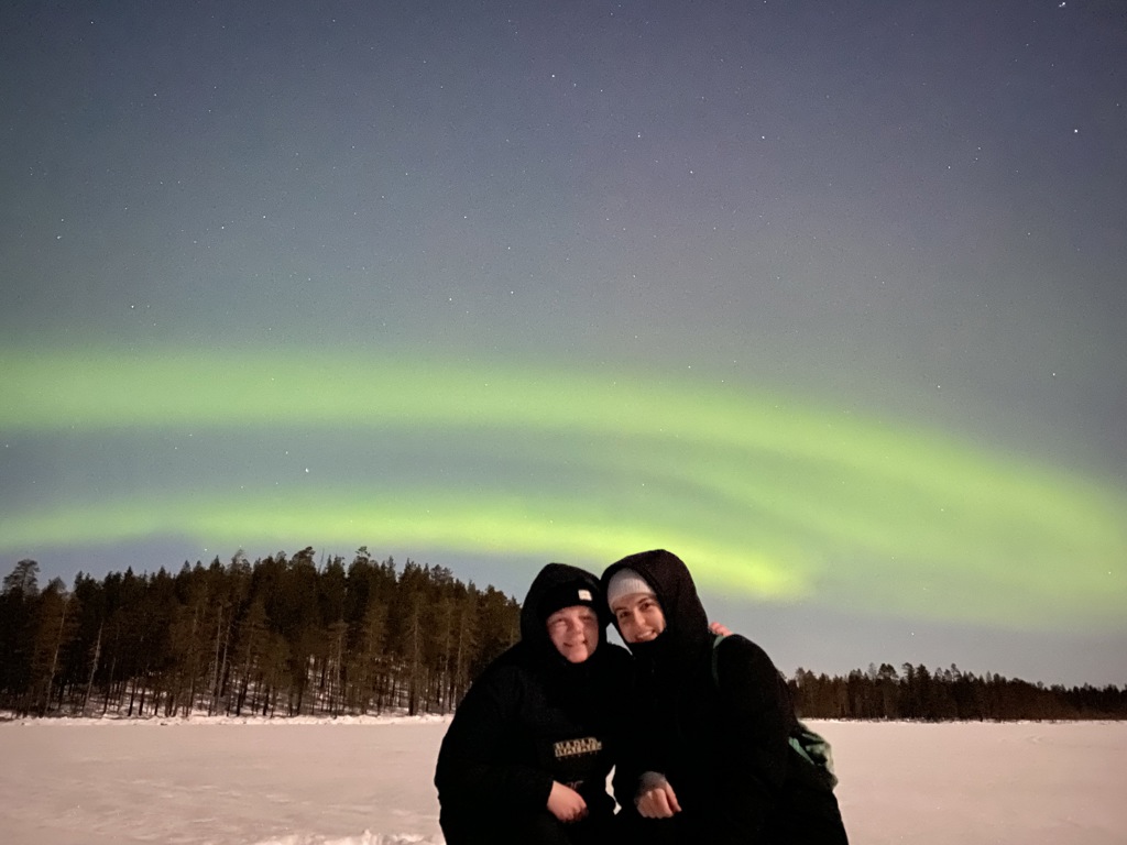 Gezin in winterkleding onder het noorderlicht tijdens een familiereis Lapland winter in Finland.