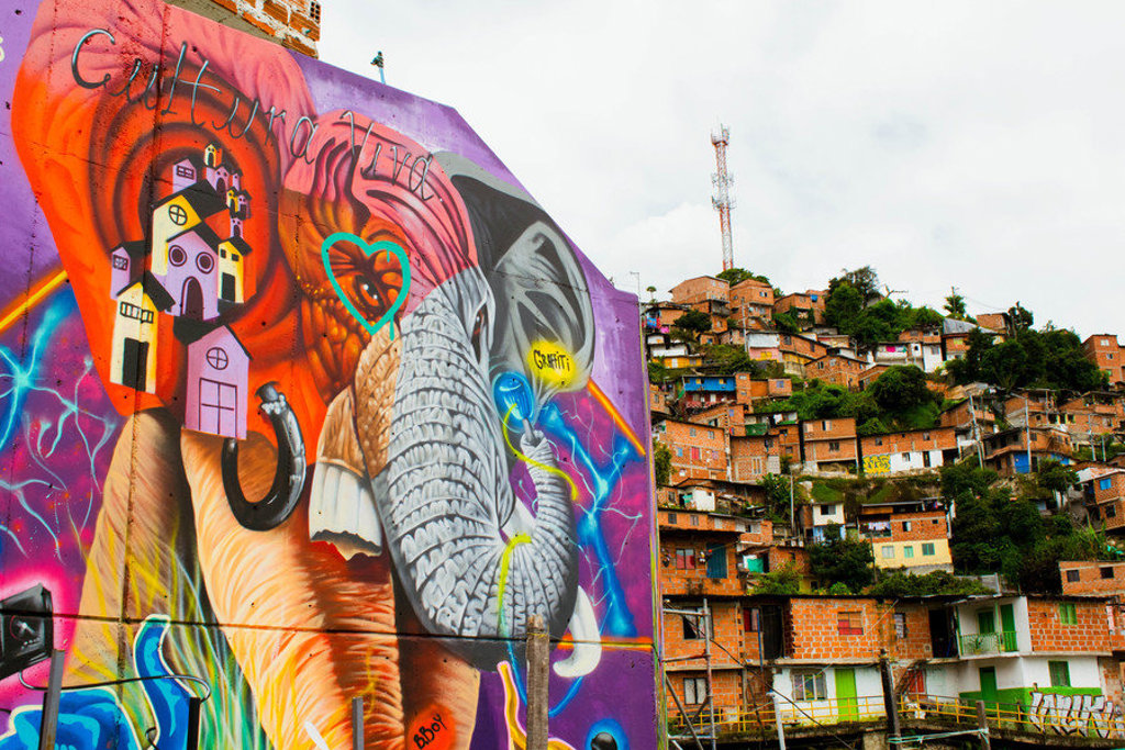 Kleurrijke graffiti van een olifant in Medellín, met huizen op een heuvel op de achtergrond.