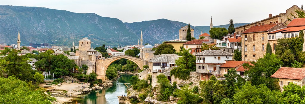 Stari Most-brug in Mostar over de Neretva, met historische huizen en bergen op de achtergrond.