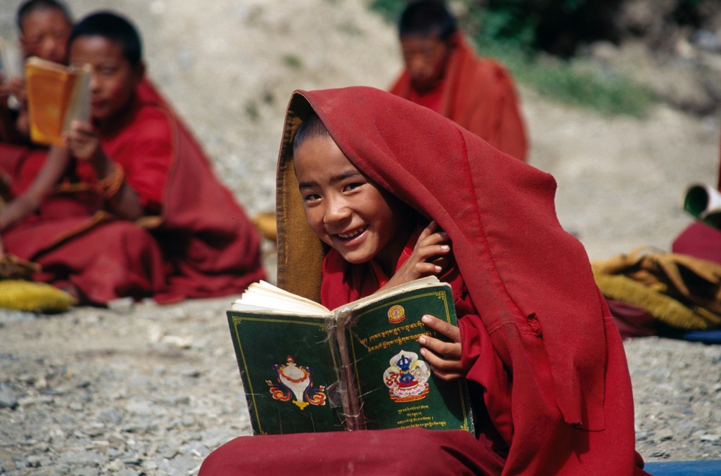 Lachende jonge monnik in Nepal met rood gewaad leest een gebedenboek tijdens familiereis Nepal.