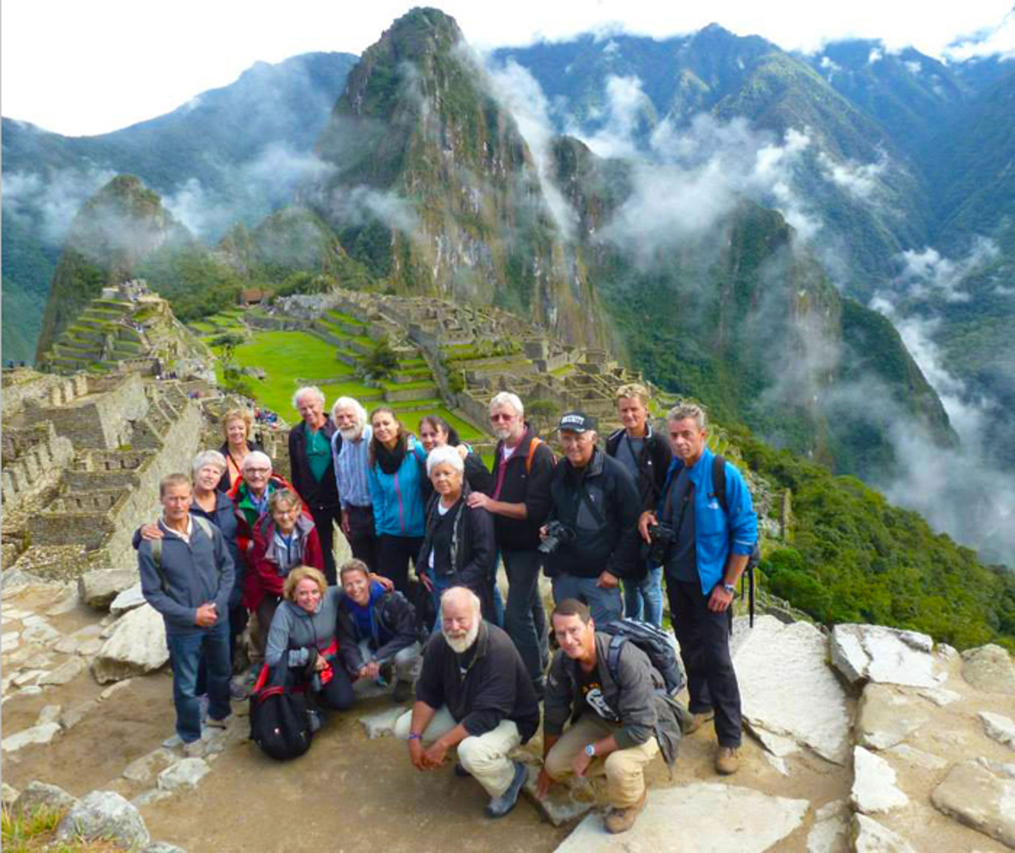 Groepsfoto van reizigers bij Machu Picchu met bergtoppen en mist op de achtergrond.