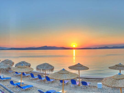Zonsondergang boven de zee bij Evia, met strandparasols en ligbedden langs het water.
