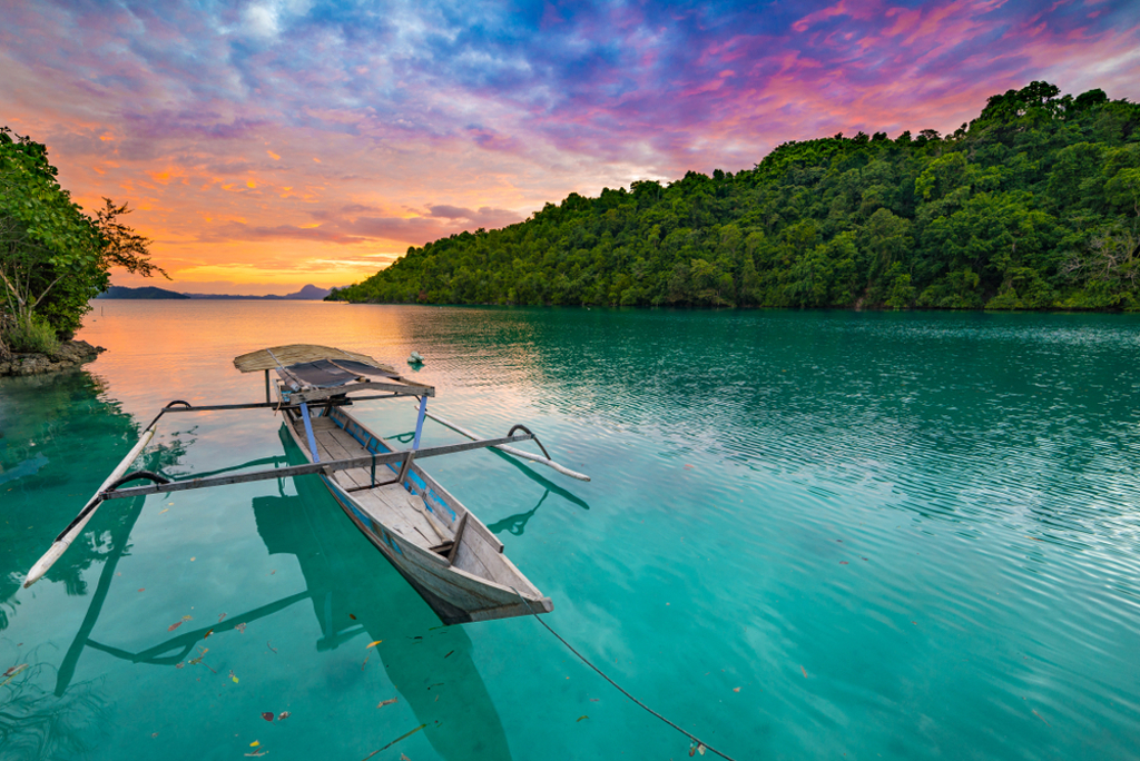Traditionele boot op turquoise zee bij groene kust in Sulawesi tijdens zonsondergang.