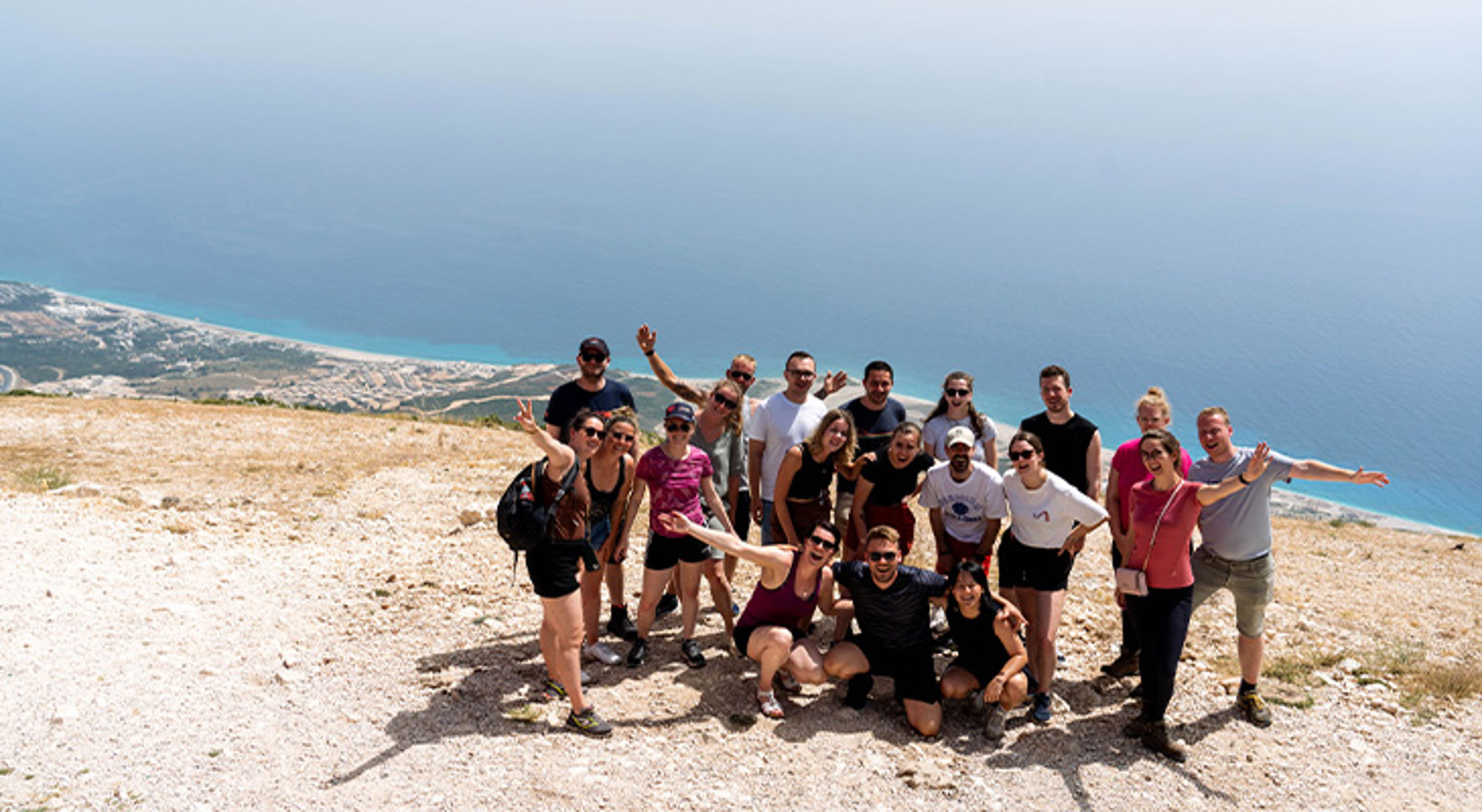 Llogara Albanië Groep reizigers poseert op een bergtop met uitzicht op de blauwe zee en kustlijn.