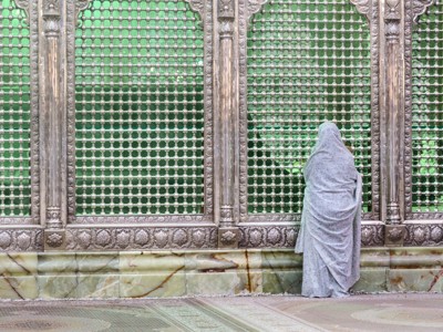 Pelgrim bidt bij het zilveren traliewerk van een heiligdom in Iran.