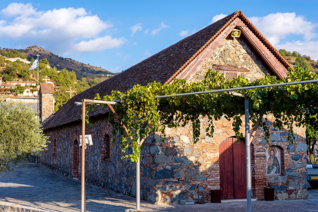 Traditionele stenen kerk op Cyprus met druivenranken en Grieks-orthodoxe kruisen in de achtergrond.