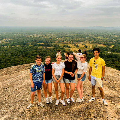 Groep jongeren op een rots met panoramisch uitzicht over het groene landschap van Sri Lanka.