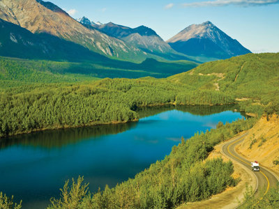 Berglandschap langs de Route Alaska met blauw meer, groene bossen en slingerweg met camper.