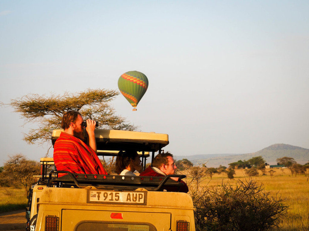 Safari in Kenia met reizigers in een jeep en een heteluchtballon boven de savanne.
