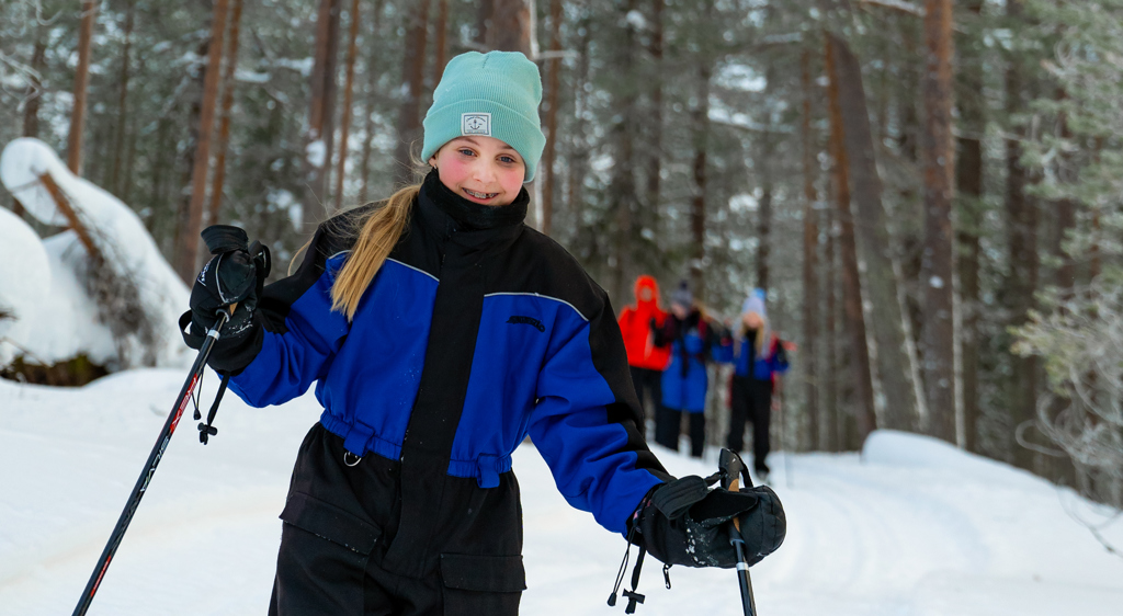 Kind op langlaufski’s in besneeuwd bos tijdens familiereis Lapland Winter in Finland.