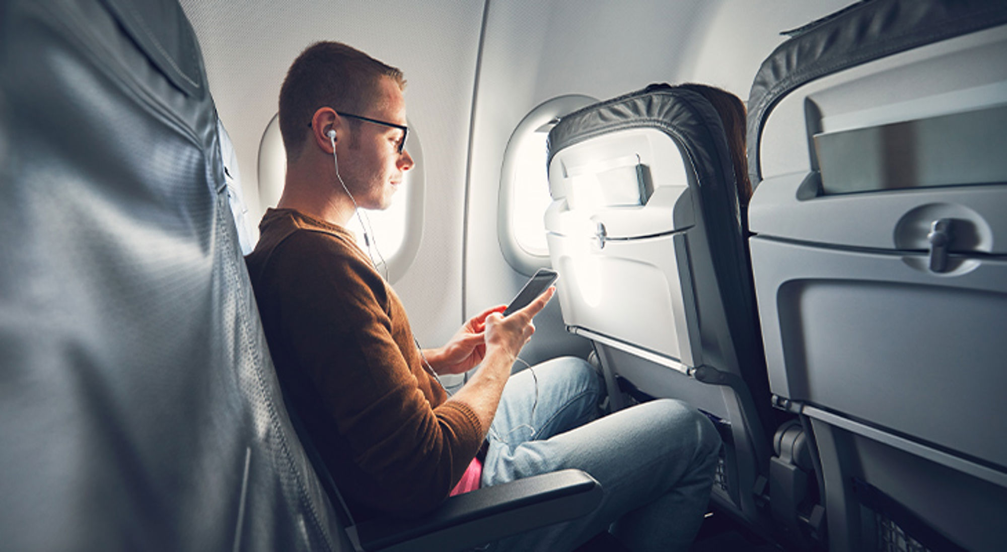 Muziek luisteren in het vliegtuig Passagier in vliegtuigstoel gebruikt smartphone met oordopjes tijdens de vlucht.