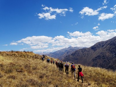 Wandelaars op bergpad in de Andes tijdens de Route Peru, met uitzicht op ruige bergen en blauwe lucht.