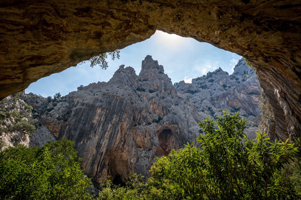 Uitzicht vanuit een grot op ruige rotsbergen en groene begroeiing op Sardinië, Italië.