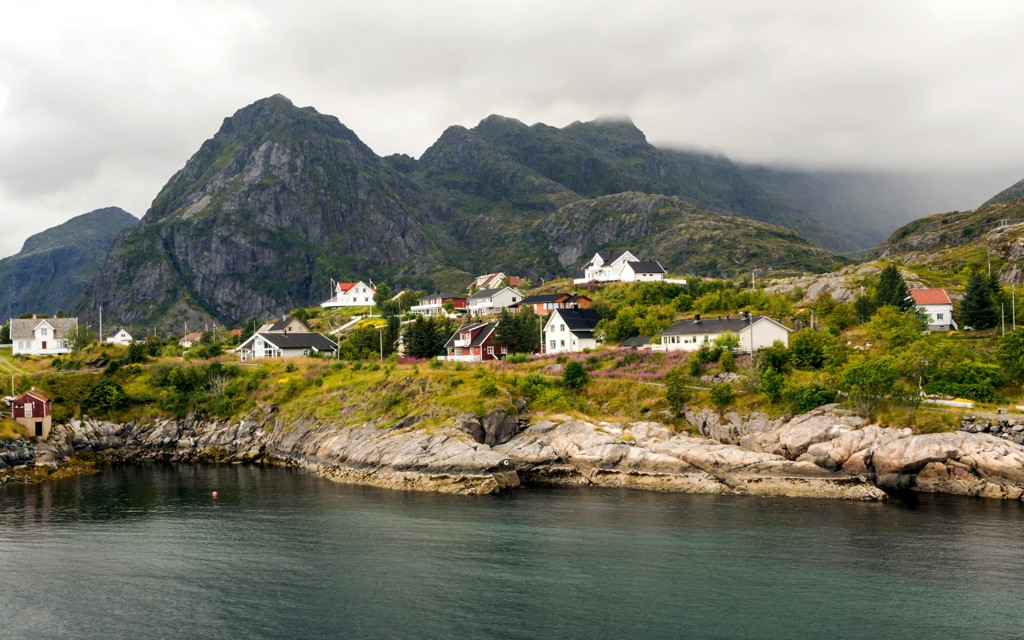 Noors kustdorp met kleurrijke huizen aan een fjord, met hoge bergen op de achtergrond.