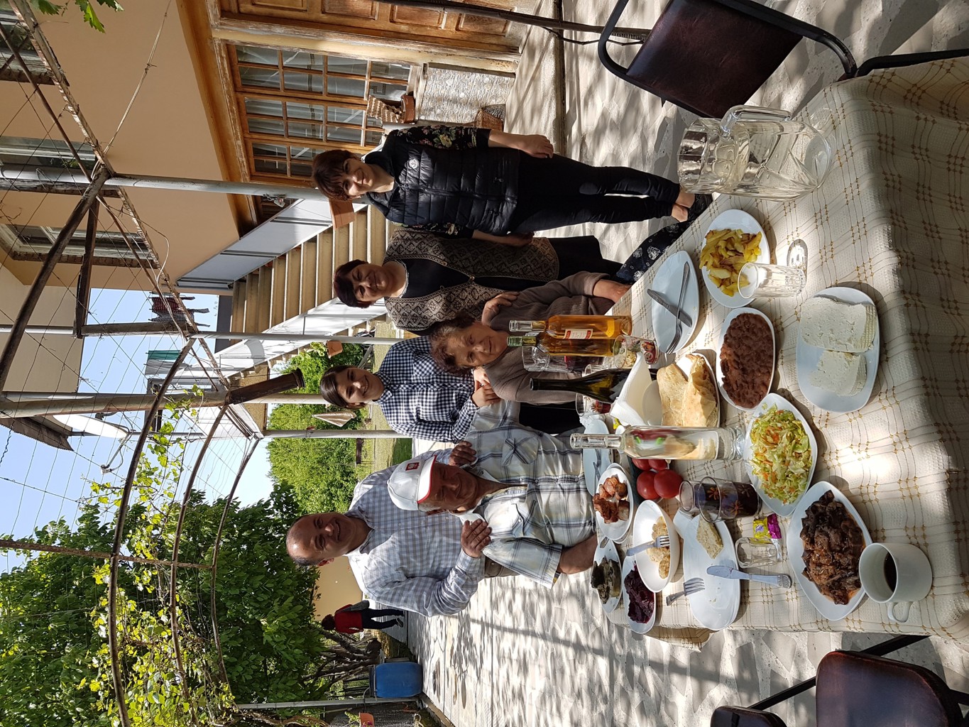 Gastgezin in Georgië poseert bij een huisgemaakte lunch met lokale gerechten en wijn in de tuin.