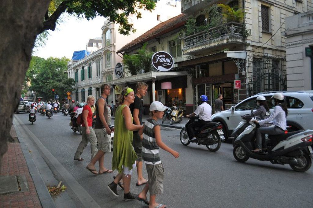 Gezin steekt een drukke straat met veel scooters over in Hanoi, Vietnam.