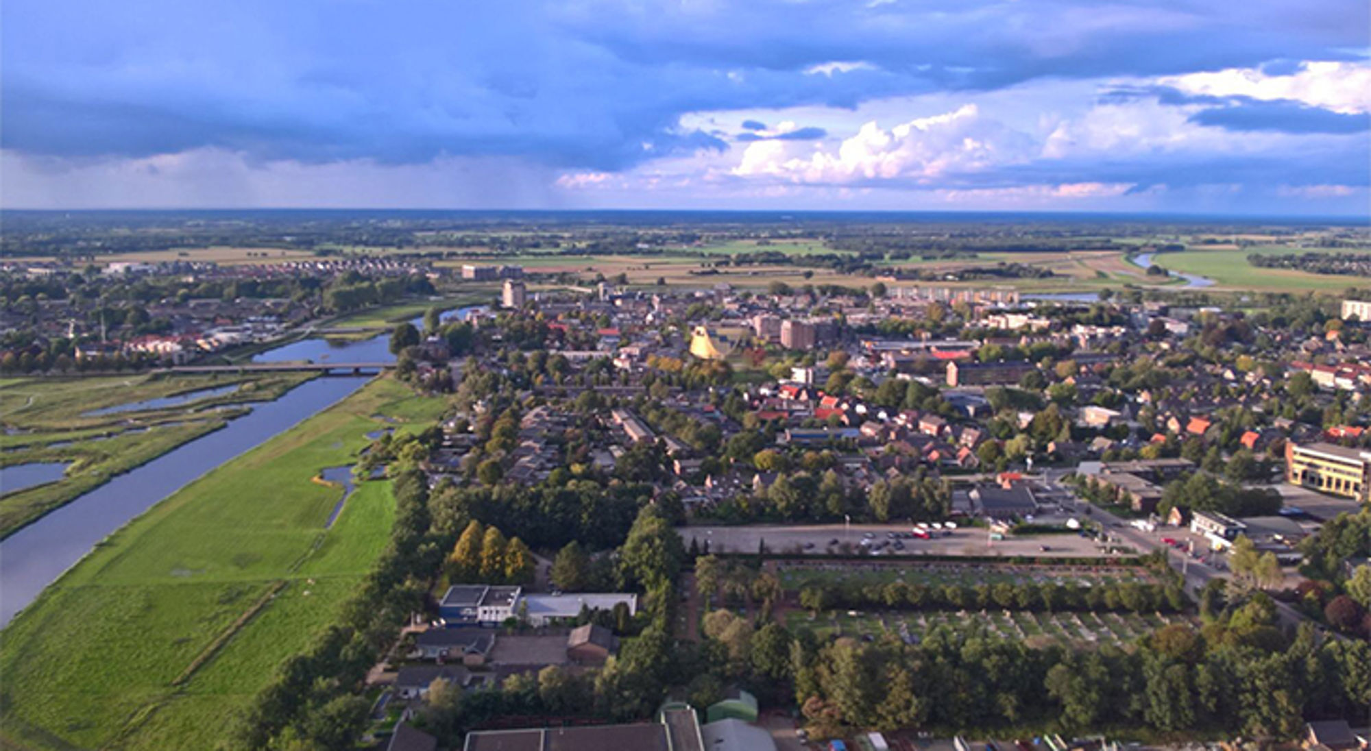 een stad aan een rivier, met woonwijken, groen en wolkenlucht.