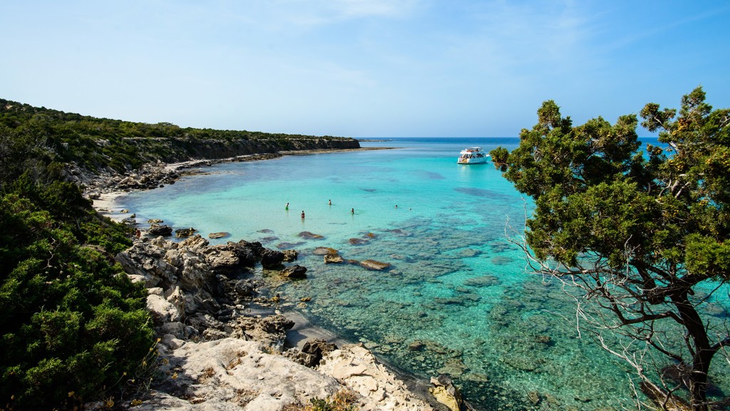 Rotsachtige baai op Cyprus met helderblauw water, zwemmers en een boot tijdens de familiereis Cyprus kort.