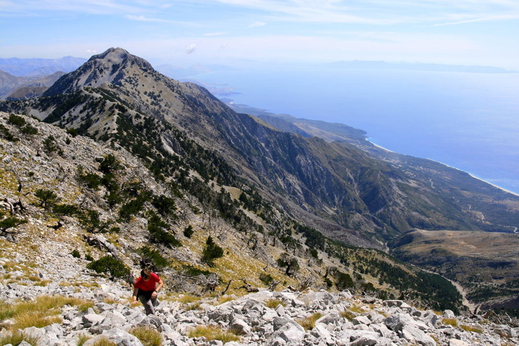 Wandelaar op bergpad met uitzicht op de Albanese Riviera en de Ionische Zee tijdens een wandelvakantie in Albanië.