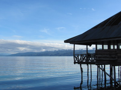 Houten huis op palen aan een rustig meer op Sulawesi, met bergen en wolken op de achtergrond.