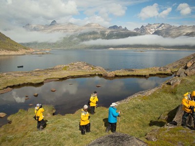 Wandelaars bij een bergmeer met fjord en mistige bergen op Groenland (dag 6 van de 15-daagse route).