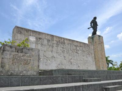 Che Guevara-monument in Santa Clara, Cuba, met bronzen standbeeld en reliëfmuur onder blauwe lucht.