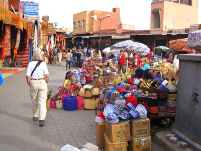 Drukke souk in Marrakech met kleurrijke tapijten, manden en mutsen langs de marktstraat.