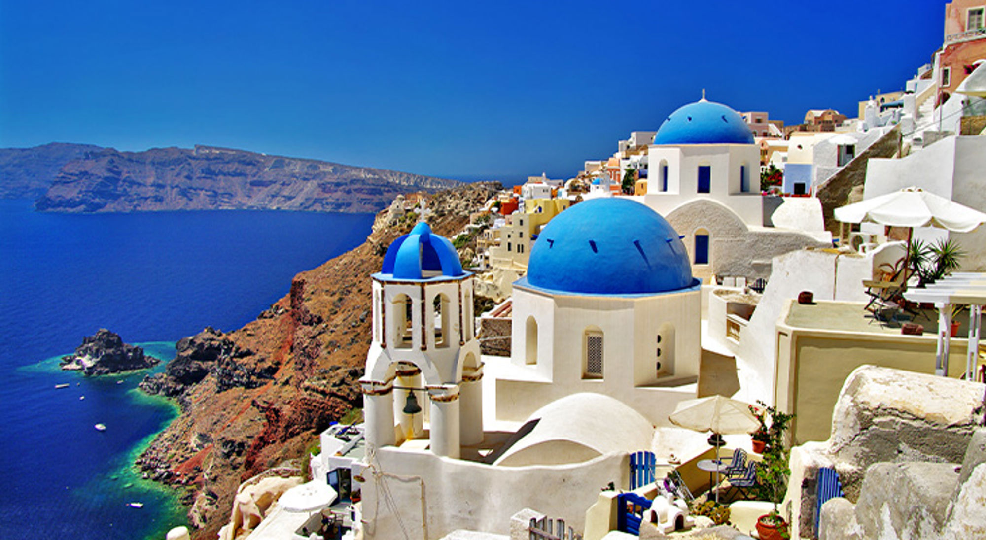 Santorini Witte huizen en kerk met blauwe koepels in Oia op Santorini, met uitzicht op zee en kliffen.