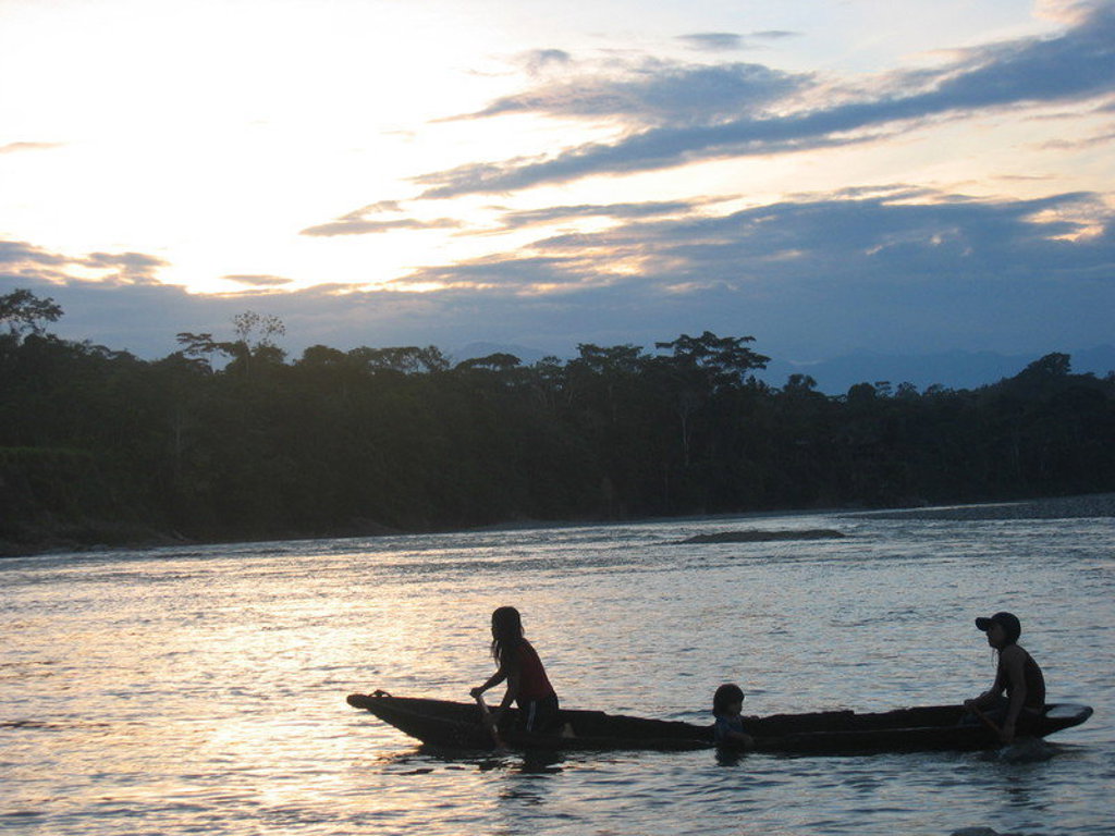 Kano met kinderen op een rivier bij zonsondergang in het Amazonegebied van Ecuador.