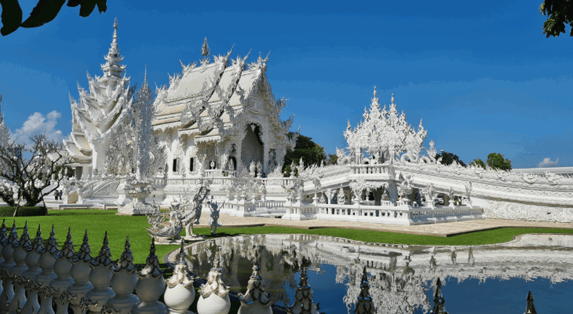 Chiang Rai Witte tempel Wat Rong Khun in Chiang Rai met weerspiegeling in vijver onder heldere blauwe lucht.