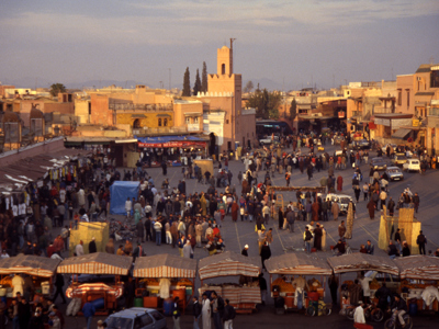 Drukke Jemaa el-Fna in Marrakech met marktkramen en de minaret van de Koutoubia-moskee op de achtergrond.