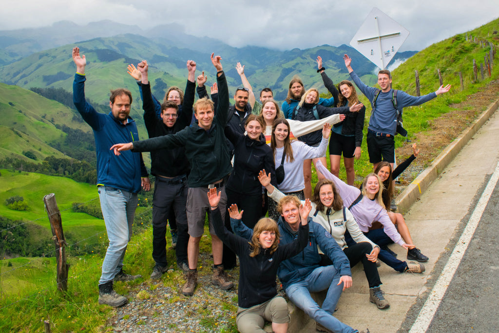 Groep 22-35ers reizigers poseert langs de weg met groene bergen op de achtergrond tijdens rondreis Colombia.