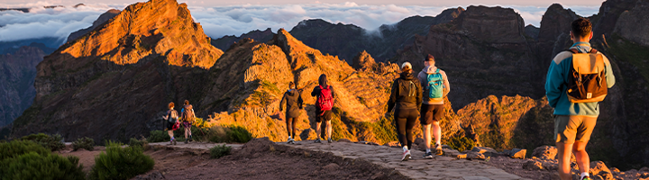 Wandelaars met rugzak op bergpad bij zonsopkomst, passend bij groeiend aanbod 22-35ers reizen.