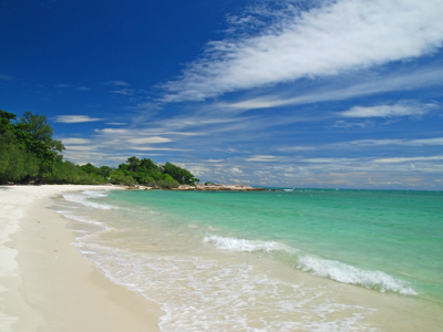 Wit zandstrand met turquoise zee en groene kustlijn langs de route Thailand.