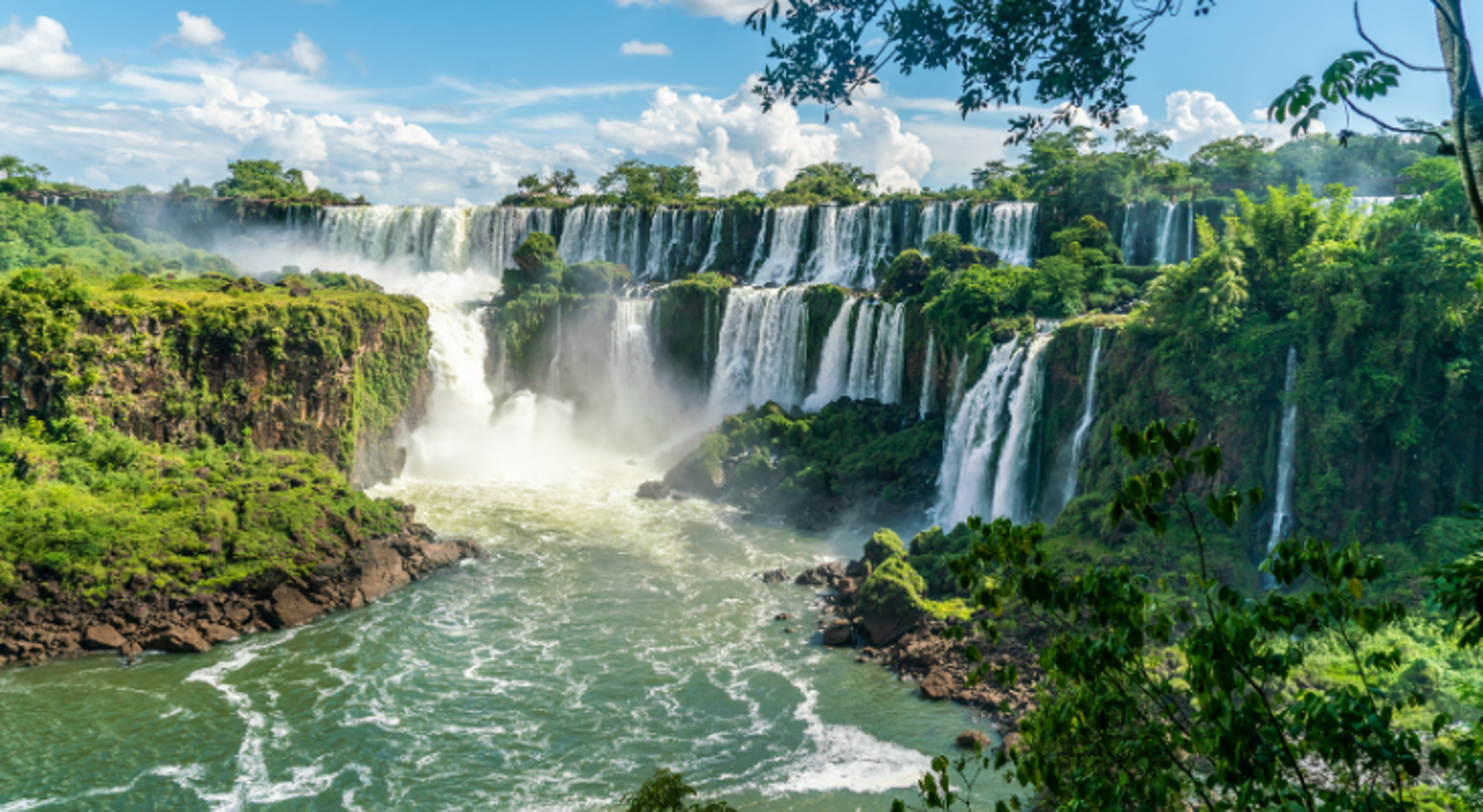 Panoramisch uitzicht op de Iguazú-watervallen met meerdere watervallen en weelderig groen langs de rivier.